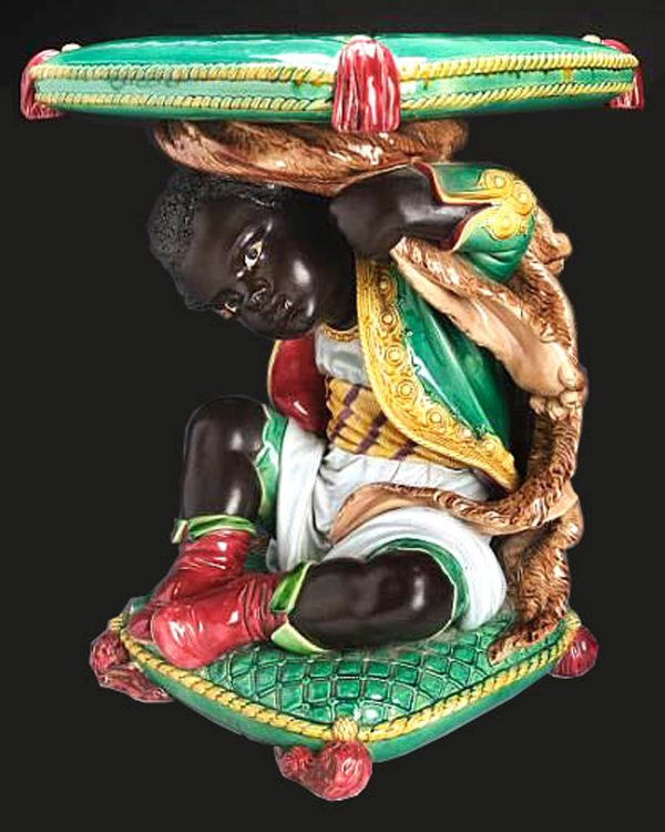 MINTON monumental Blackamoor garden seat depicting: MINTON monumental Blackamoor garden seat depicting a Blackamoor boy with lions skin over shoulders seated on a green cushion with red/pink tassels supporting a similar cushion on his head which serves