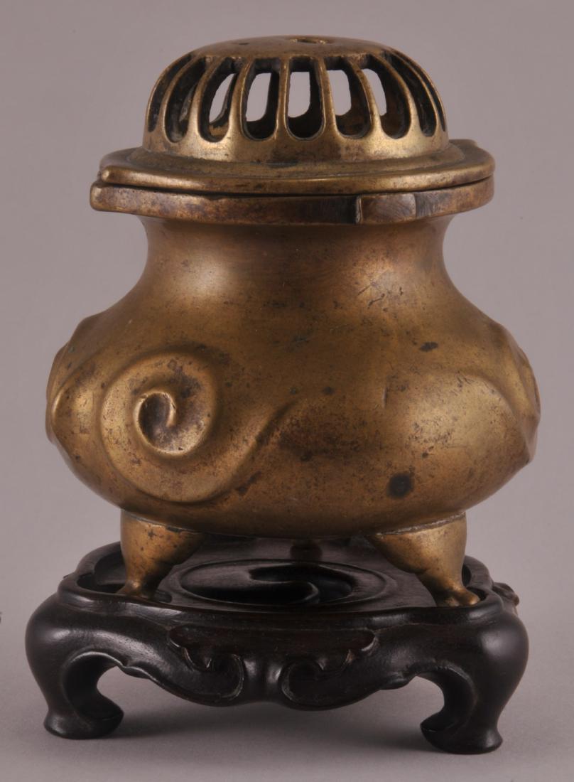 19th century Chinese Bronze three footed covered censer: 19th century Chinese Bronze three footed covered censer with raised scroll decoration. Carved wood fitted base. 4-1/2" high with base.