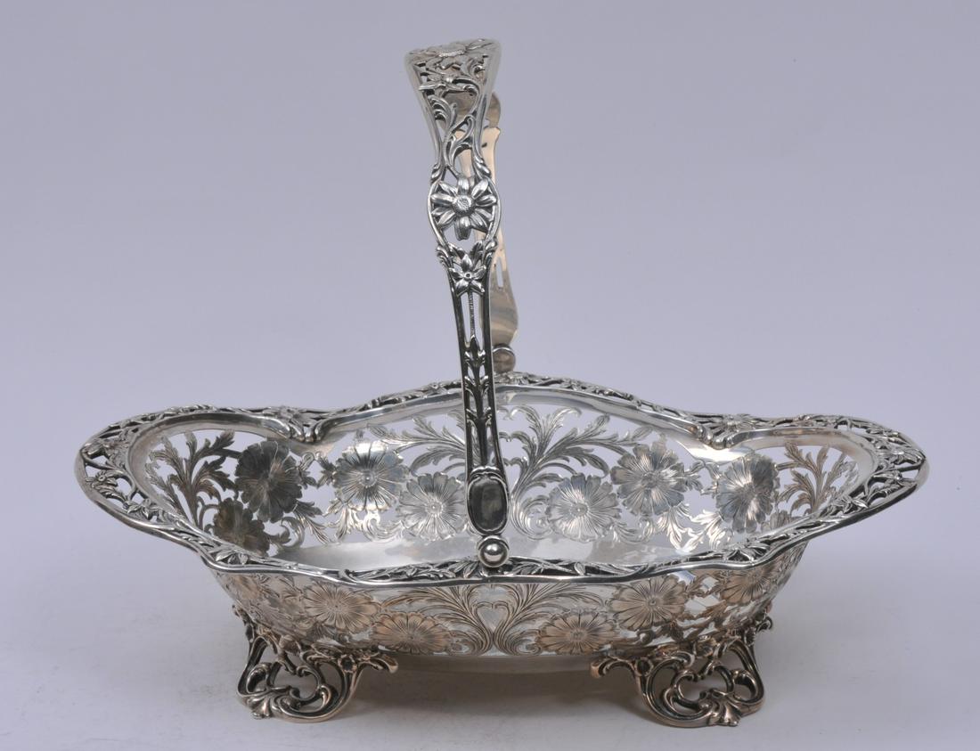 Large sterling silver pierced decorated footed handled: Large sterling silver pierced decorated footed handled basket. Pierced floral design with pierced leaf scroll feet. RW makers mark. 14" long. 10-1/2" wide. 42.1 ozt. Good condition.
