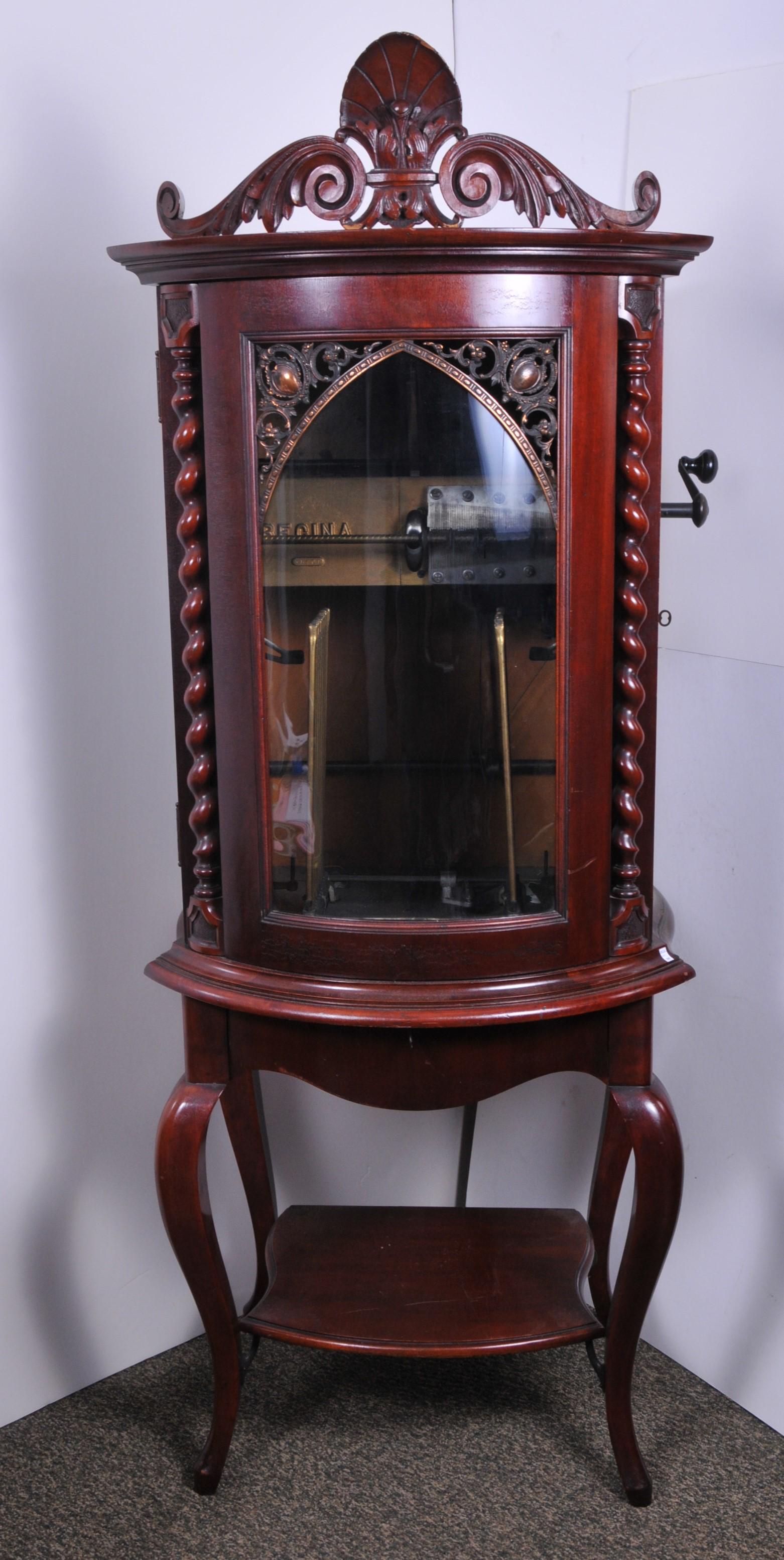 Regina Music Box. Style 35. Mahogany case with curved: Regina Music Box. Style 35. Mahogany case with curved front and twist columns. Applied cast frame and foliate crest. Single storage drawer and shelf. Twelve disc auto changer, #51401. Includes 35 musi