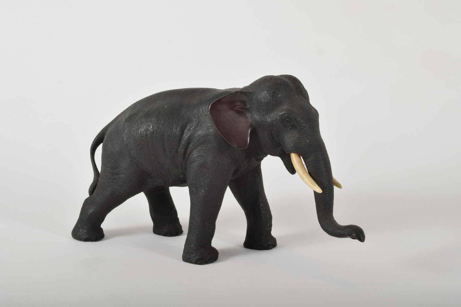 Asian Bronze Elepehant Sculpture: Asian Bronze Elephant Sculpture. Textured skin with bone tusks. Marked to underside of belly. 7” x 5” x 12”.