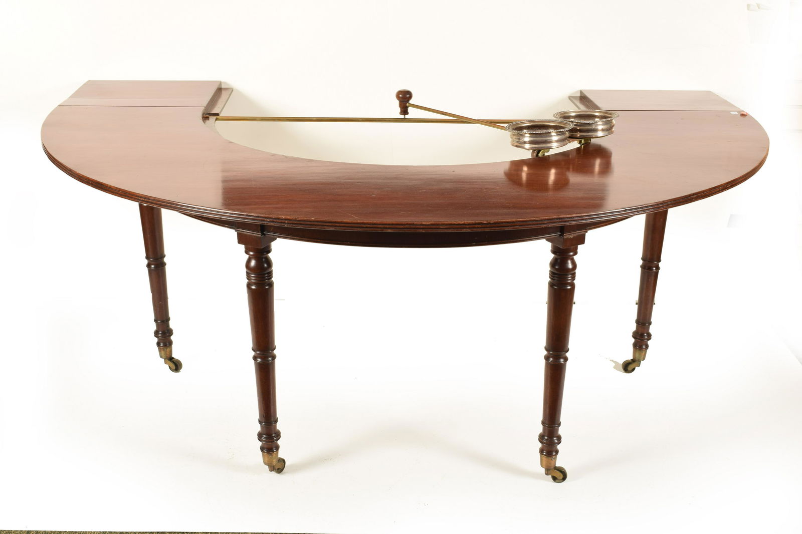 Sheraton Style Mahogany Hunt-Wine Table: Sheraton style mahogany Hunt-Wine table. ½” round shape with drop leaf removable center section. Turned legs. Attachable brass and silver-plate decanter holder. Table constructed in antique
