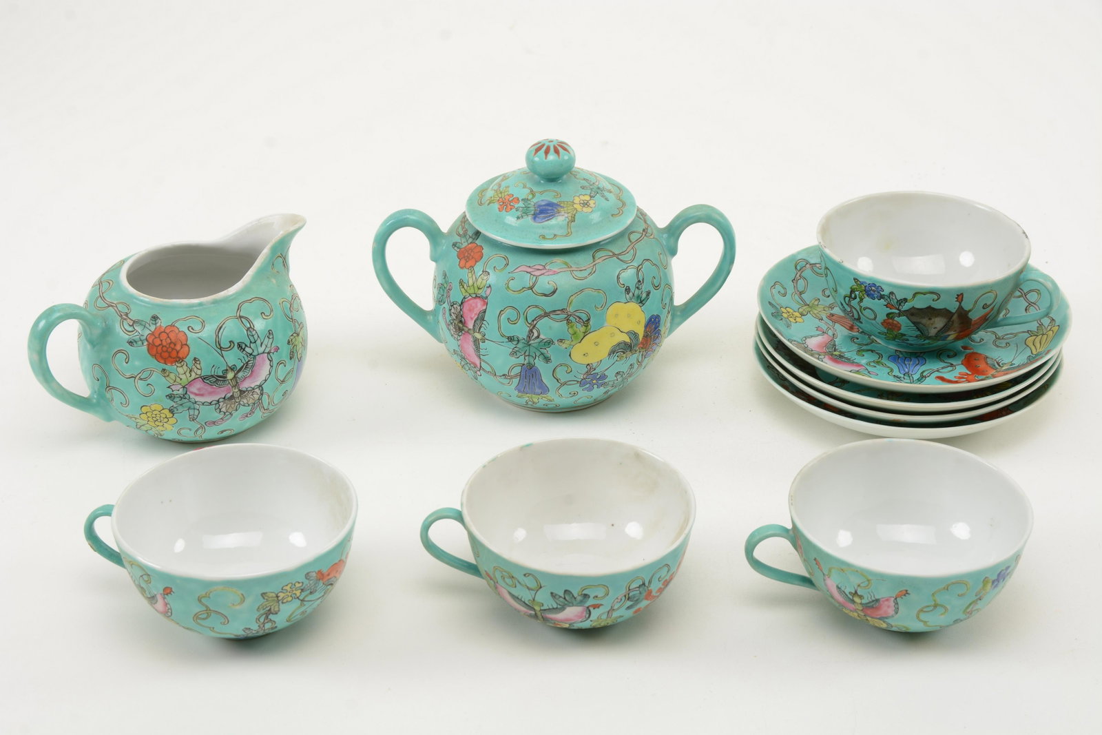 Chinese Ten-Piece Tea Set. Moth Decorations on: Ten-Piece Tea Set. Moth Decorations on turquoise ground with flowers and scroll work. Includes 4 cups and saucers, creamer and sugar. Some glaze slips, dirtying and general wear consistent with age. S