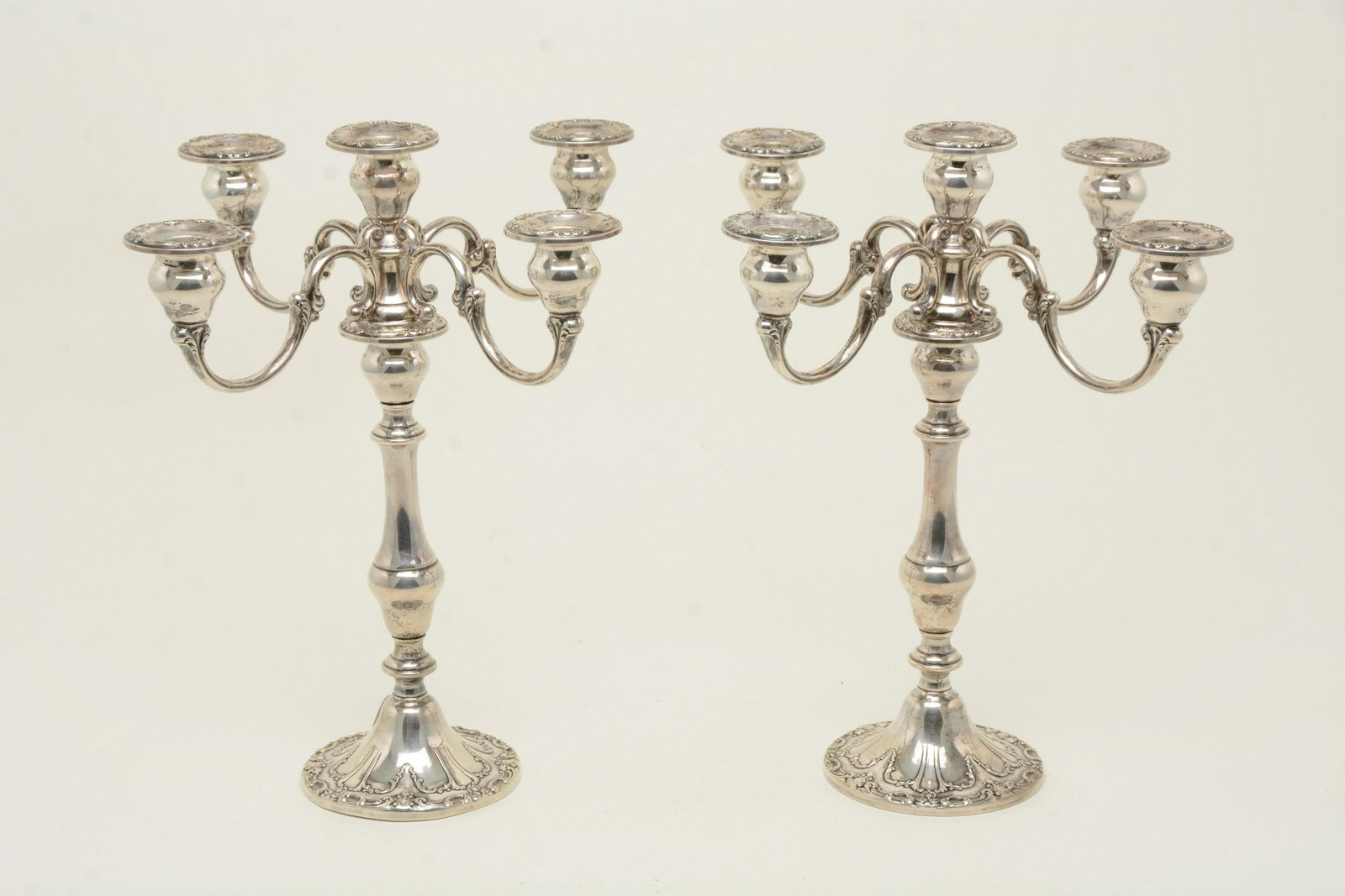 Pair of Gorham weighted sterling silver candelabra.: Pair of Gorham weighted sterling silver candelabra. 4-arm candelabras with scrollwork decoration and embossed bases. One stands slightly bent. Minor denting to base. 13.25” high.