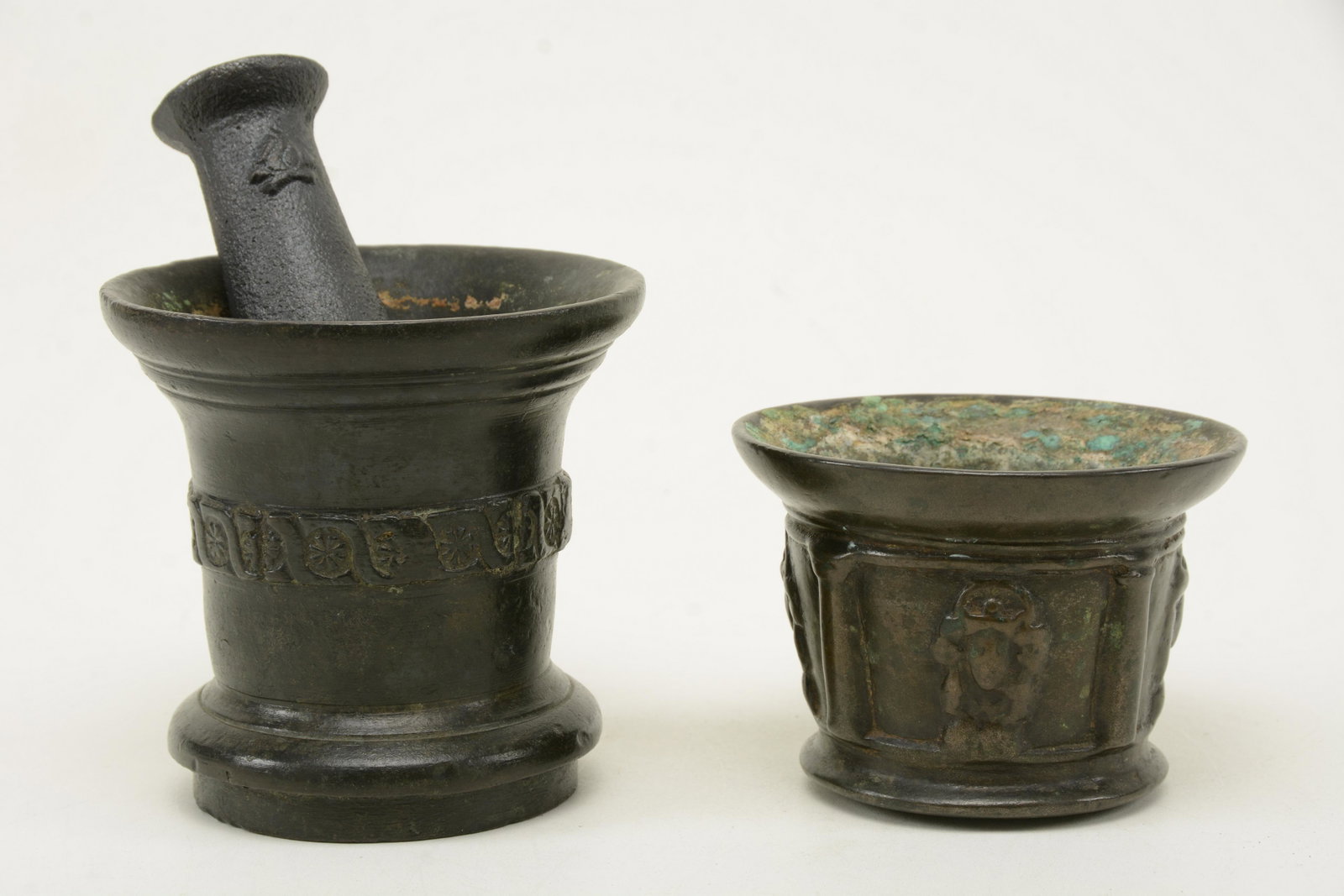 Two Bronze Mortars, China/Southeast Asia, possible 17C: Two Bronze Mortars, China/Southeast Asia, possible 17C or older, the larger decorated with a band of florets and the other with faces in relief (rubbed from age), with modern iron pestle. Height 6 in.