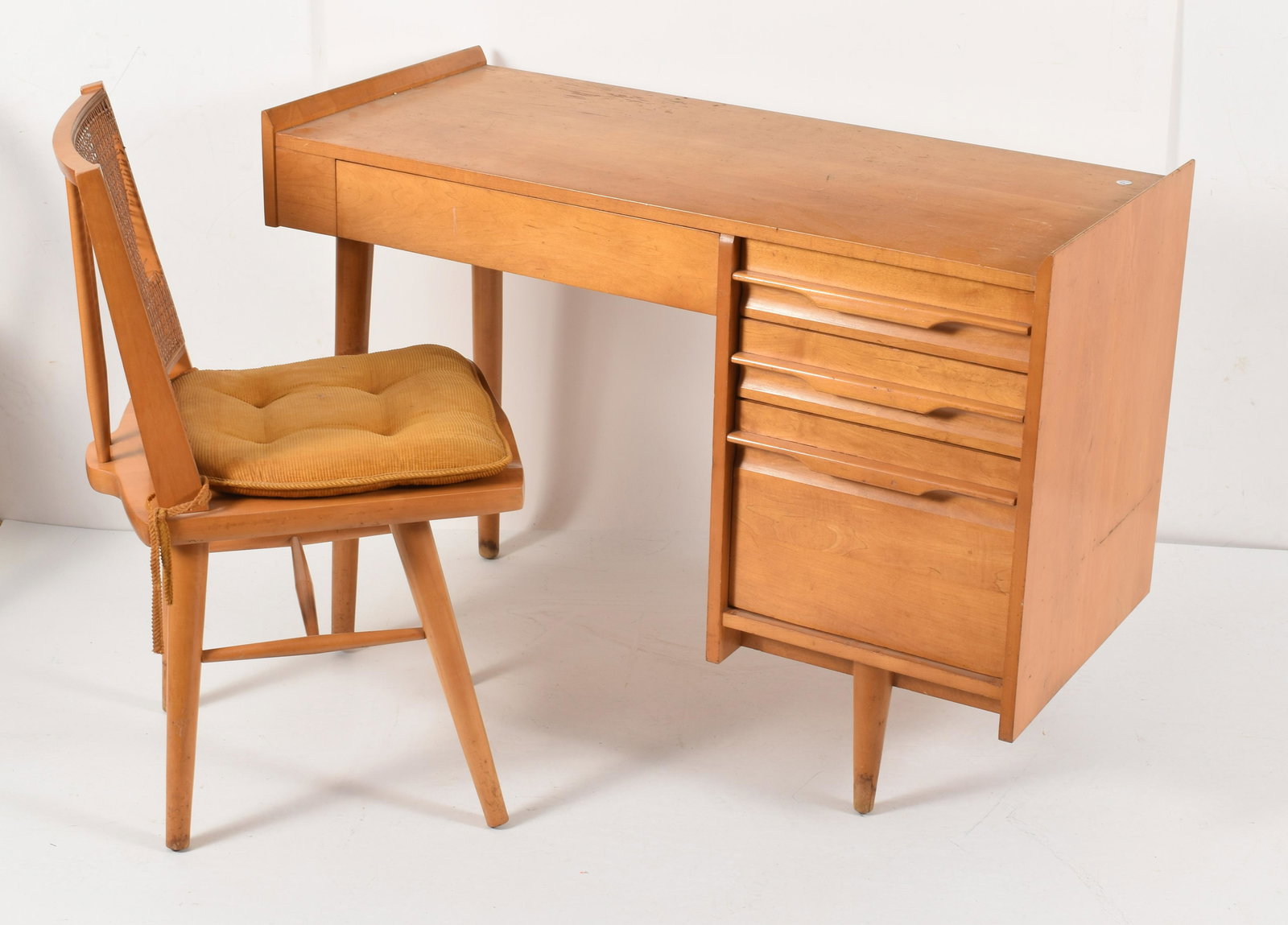 Haywood Wakefield Mid-Century-Modern blonde desk and: Haywood Wakefield Mid-Century-Modern blonde desk and cane back chair. Damage to chair cane, water staining to feet. Height 30in, width 42in, depth 19in.