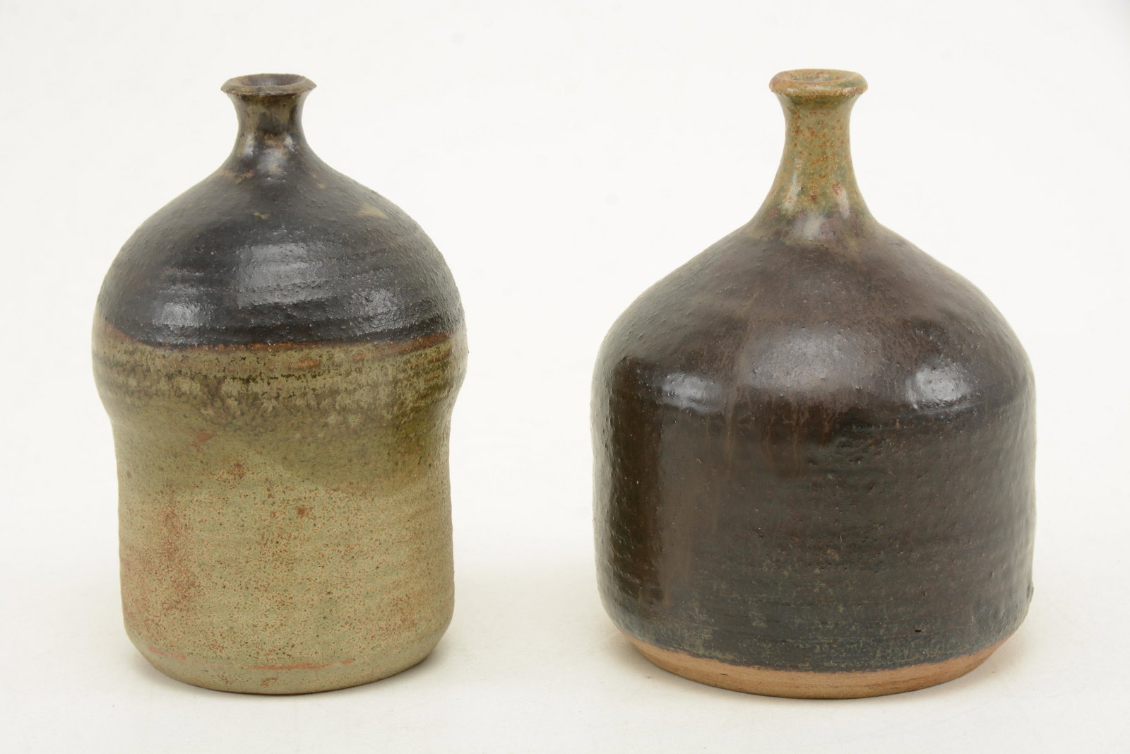 2 Japanese studio pottery bottle form vases. Narrow: 2 Japanese studio pottery bottle form vases. Narrow necks with flared rims. Deep brown and green tone glazes. Each bears artist hallmark to side of base. 5.75in height of largest.