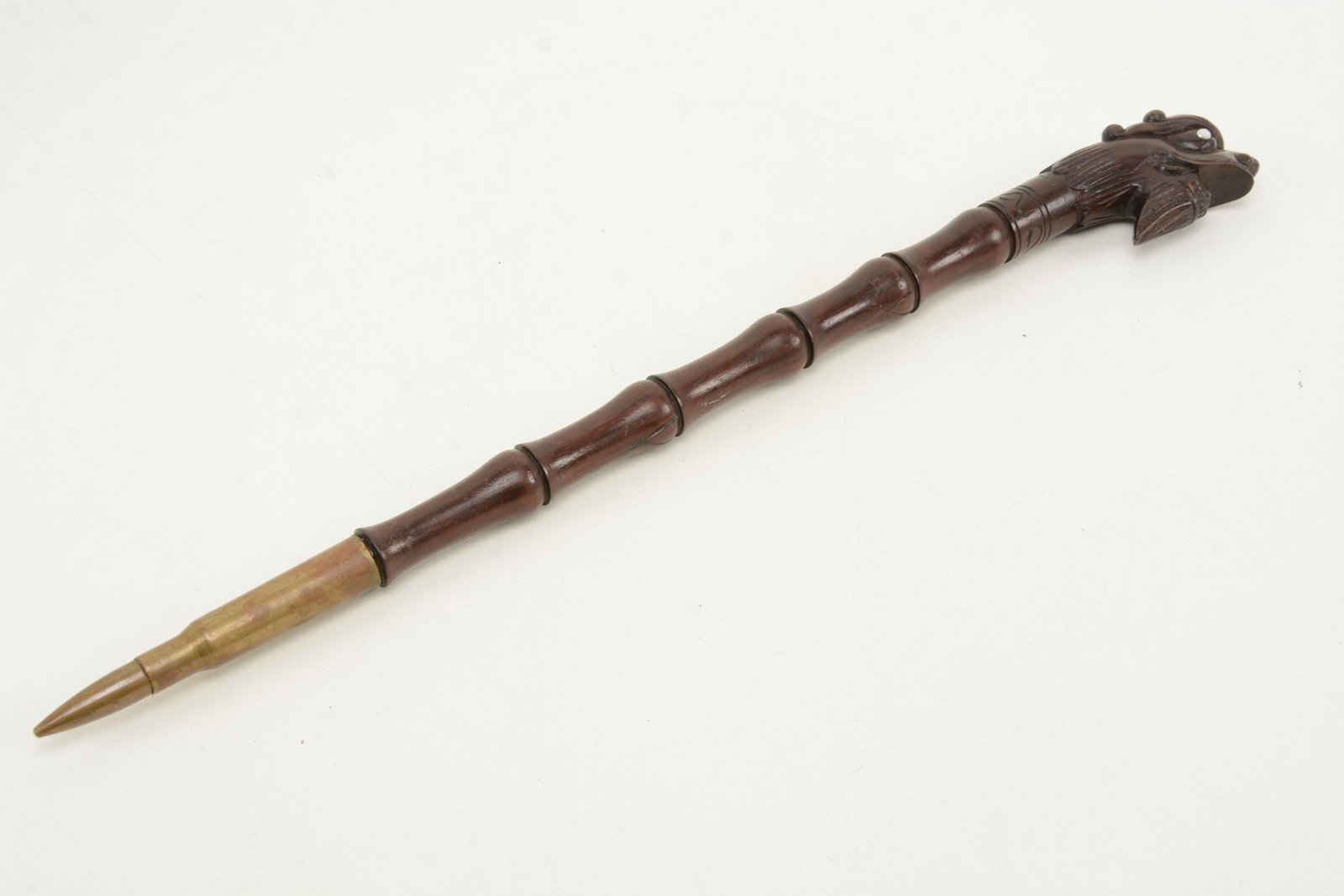 Trench art mid-20th Century, carved rosewood short: Trench art mid-20th Century, carved rosewood short staff or crop. The shaft turned and carved as bamboo with a dragon head and mounted with a large caliber bullet and casing. Length 21.5 in