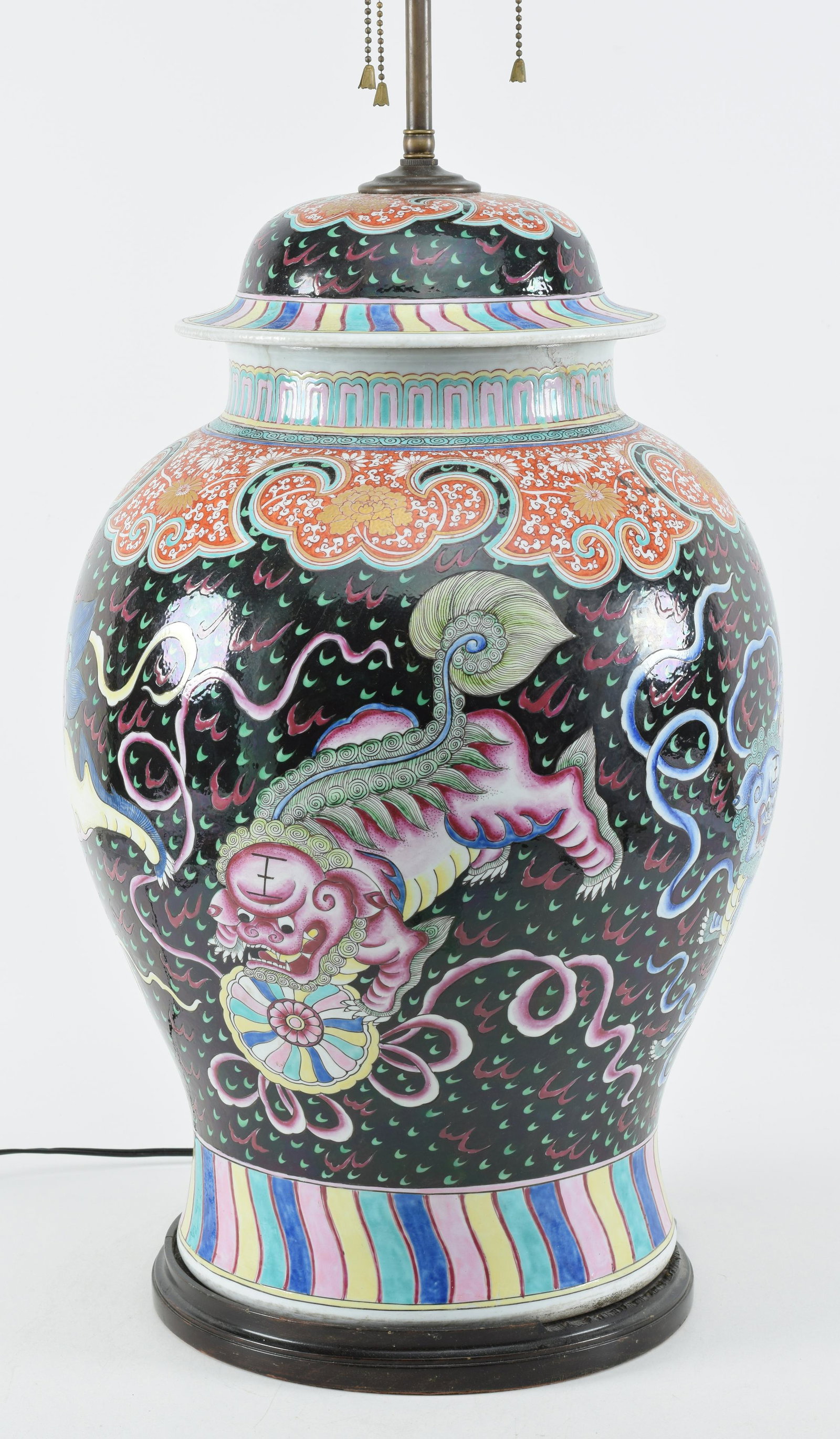 Porcelain covered jar. China. 19th century. Baluster form. Decoration of famille rose foo dogs on a: Porcelain covered jar. China. 19th century. Baluster form. Decoration of famille rose foo dogs on a black ground. Rainbow and iron red and gilt chrysanthemum borders. Cracks. Drilled. Mounted as lamp.