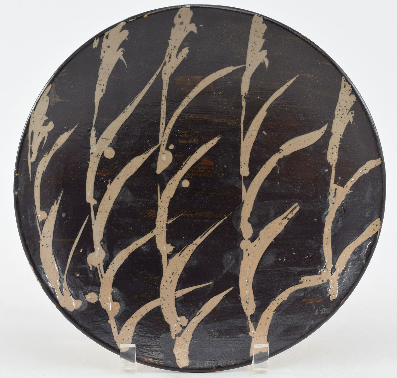 Stoneware plate. Japan. Mid-20th century. Mashiko ware. Attributed to Shoji Hamada. Cream colored: Stoneware plate. Japan. Mid-20th century. Mashiko ware. Attributed to Shoji Hamada. Cream colored autumn grasses on a brown ground. 11in.
