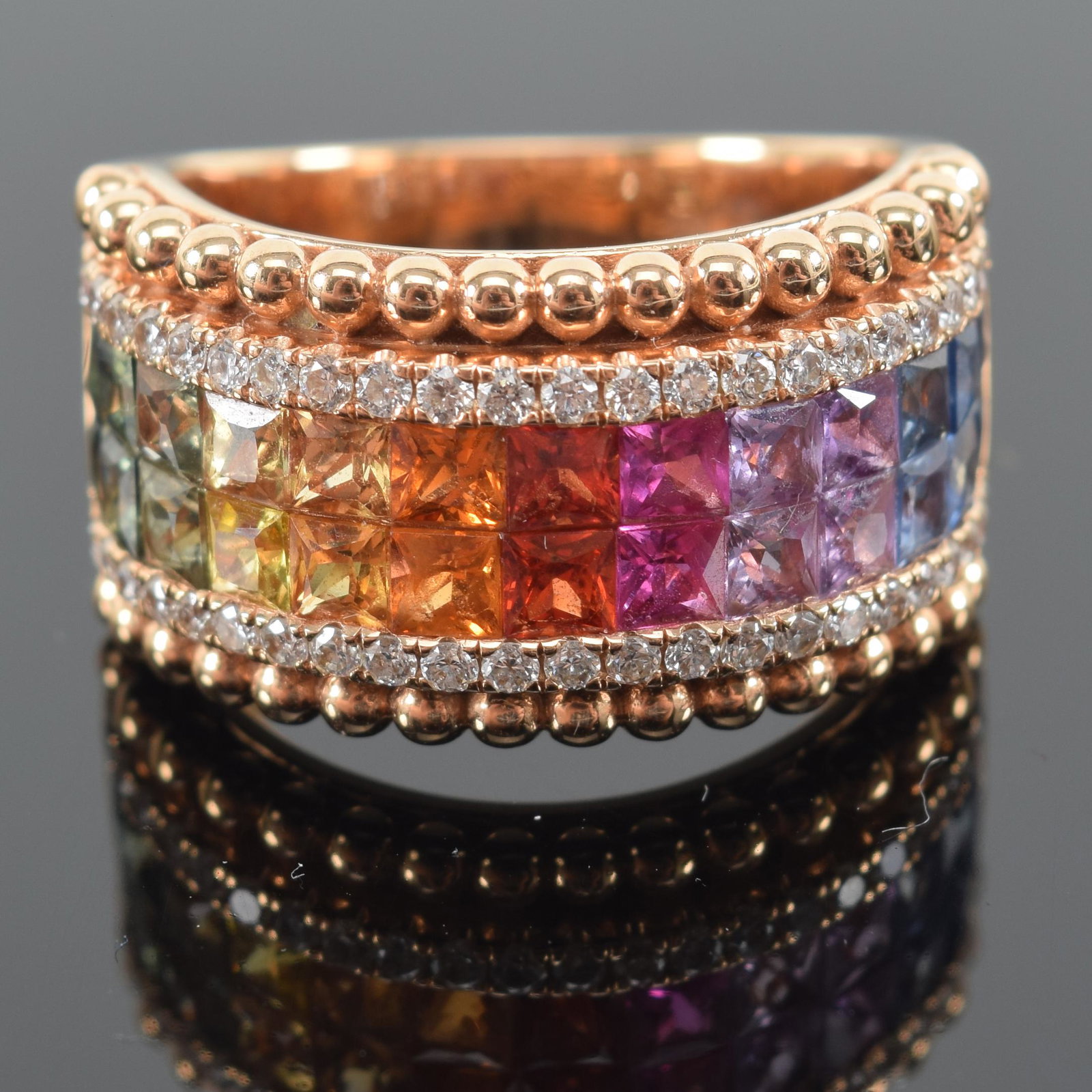 18K gold band mounted with rubies, sapphires, diamonds, emeralds, and topaz. Bead borders. Marked: 18K gold band mounted with rubies, sapphires, diamonds, emeralds, and topaz. Bead borders. Marked 750, "M" in a square, "DO" and serial numbers. Approx ring size: 6.25. 10.7 grams.