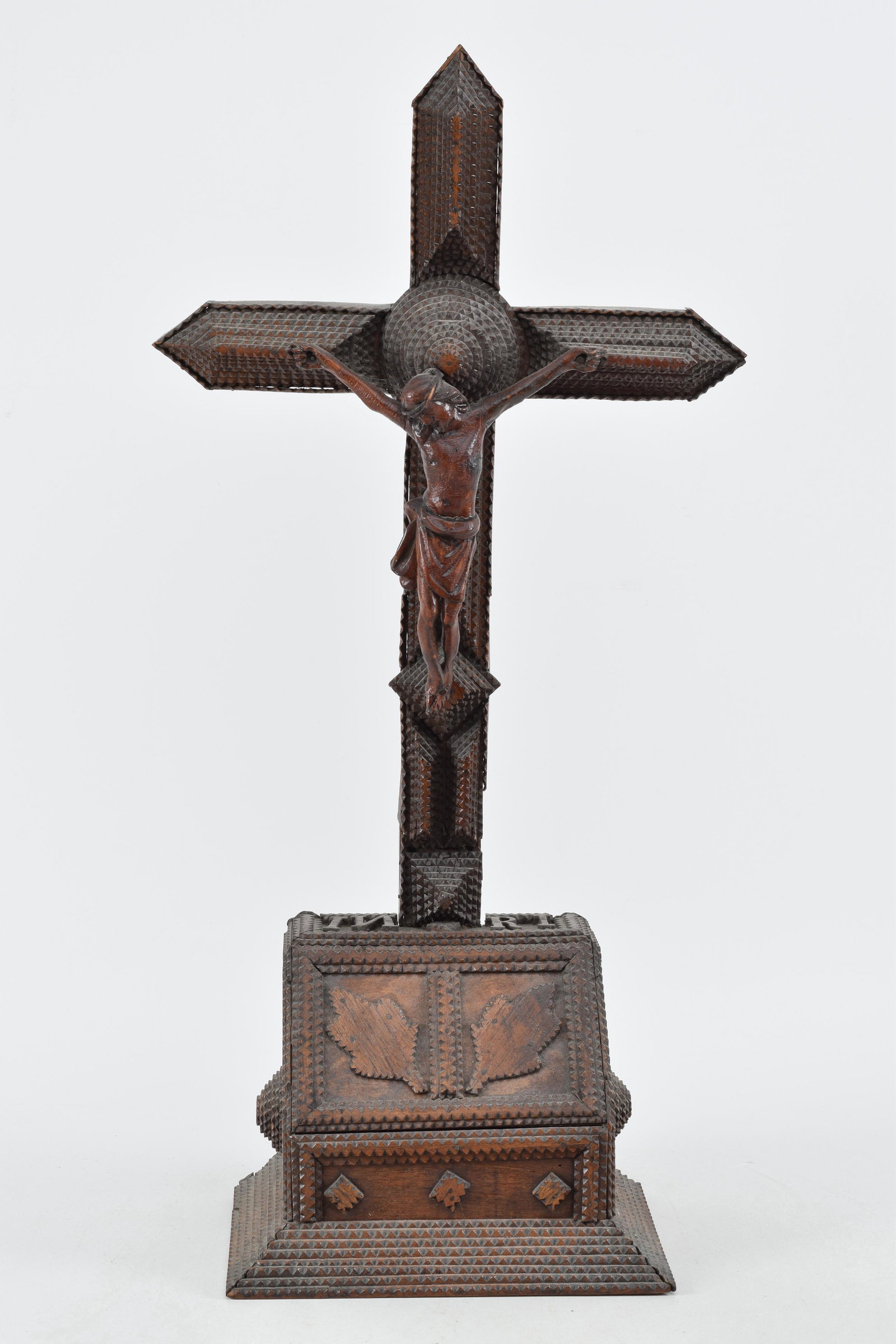 Tramp art notch and chip carved crucifix raised on a paneled plint. Full body savior on a laminated: Tramp art notch and chip carved crucifix raised on a paneled plint. Full body savior on a laminated cross. The plinth with oak leaves and raised medallions. Height 26 in. Good condition with repairs t