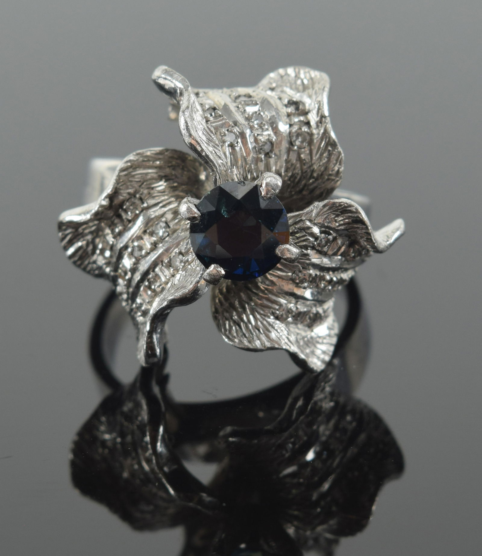 18K gold sapphire and diamond mounted flower form heavy ring. Round sapphire approx. 5.5mm. Marked (1 of 7)