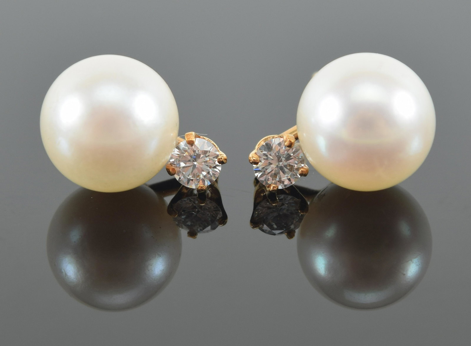14K Gold, cultured pearl, and diamond earrings; the pearl studs atop a prong set round brilliant cut: 14K Gold, cultured pearl, and diamond earrings; the pearl studs atop a prong set round brilliant cut diamond, 2.17 grams.