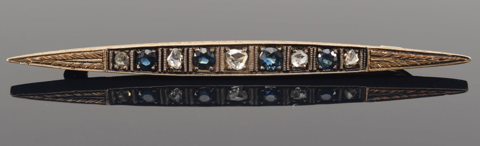 Antique gold rose mine cut diamond and sapphire mounted bar pin. 5 mine cut diamonds and 4: Antique gold rose mine cut diamond and sapphire mounted bar pin. 5 mine cut diamonds and 4 sapphires. Engraved decoration along top and sides. Probably silver back plate. Tests 14K. 3 3/8in long. 11.5