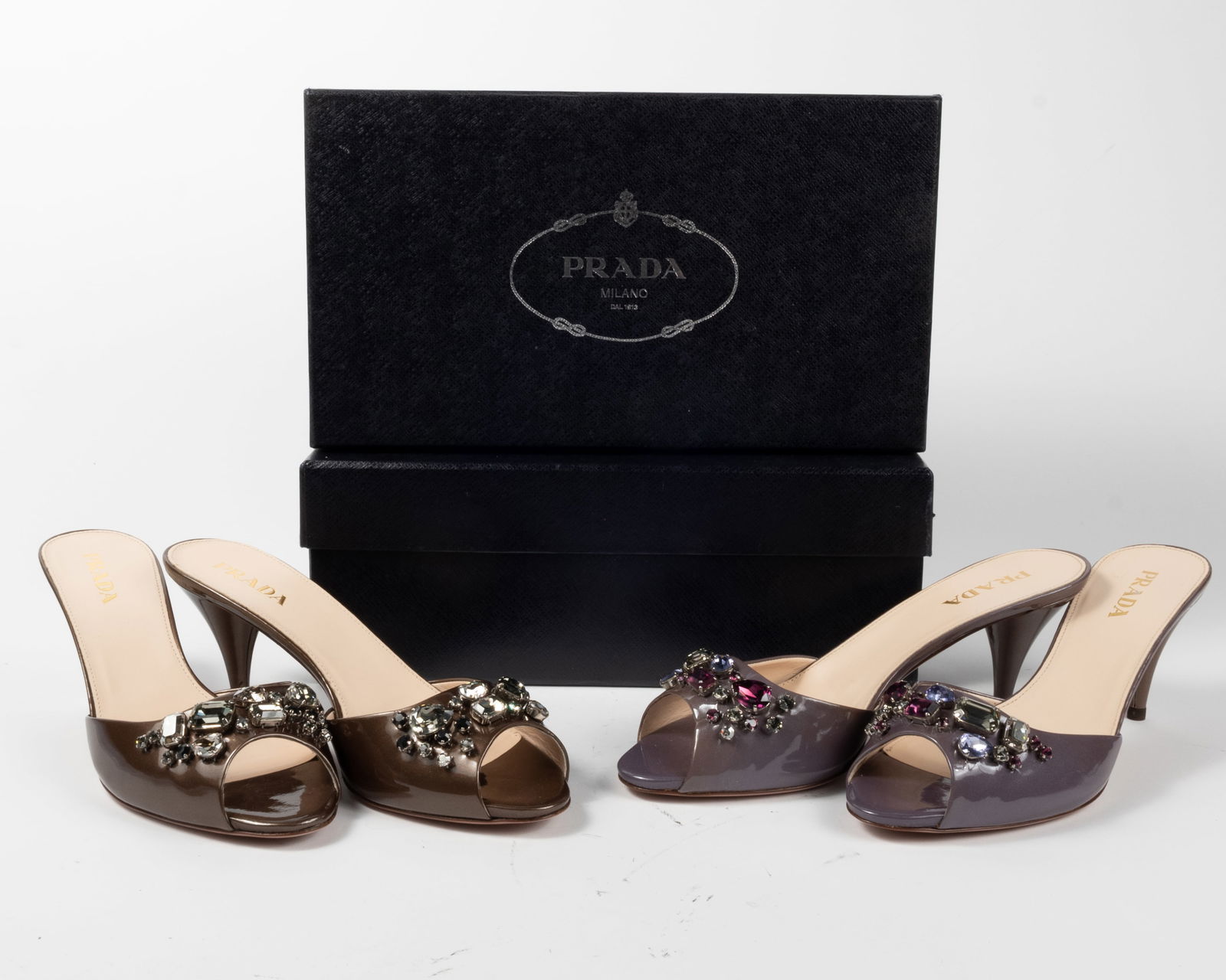 Two pairs Prada satin leather high heeled peep toed mules. In original boxes with dust bags. (1): Two pairs Prada satin leather high heeled peep toed mules. In original boxes with dust bags. (1) Deep lavender color with taupe toed heel. Heel height 3", size 38-1/2. (2) Pewter color with rhinestone