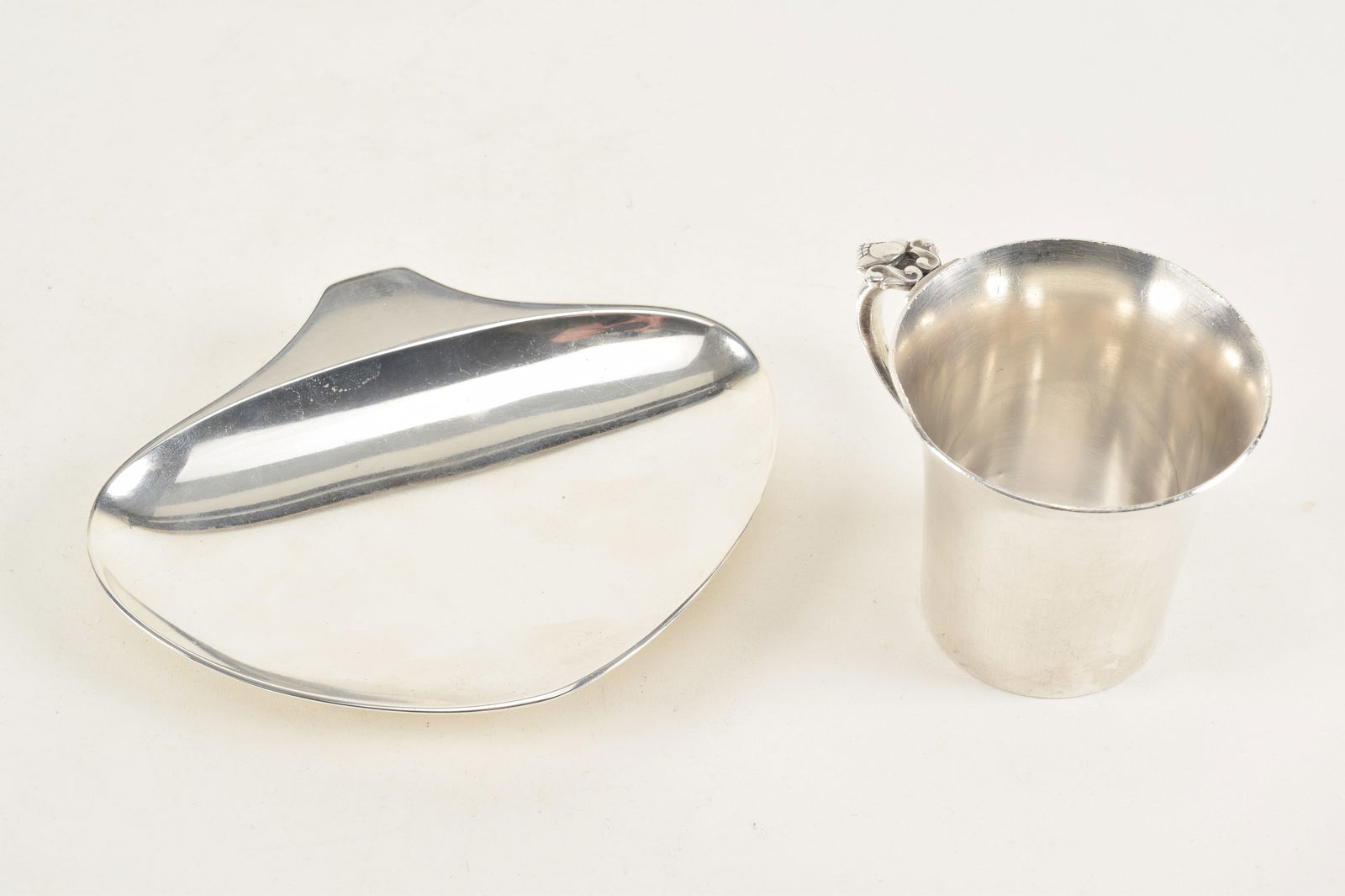 Georg Jensen Danish modern sterling silver pieces. 1) Henning Koppel spade form ring dish. Marked on: Georg Jensen Danish modern sterling silver pieces. 1) Henning Koppel spade form ring dish. Marked on reverse. 5.5in wide. 2) Child's cup with acorn handle. Small dents to rim and foot. Marked. 8.5 ozt