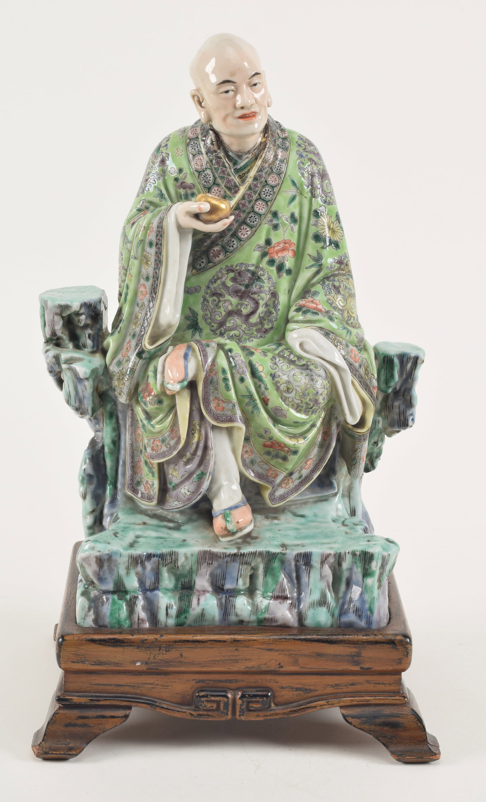 Porcelain figure of a Luohan. China. 19th century. seated figure with famille verte decoration.: Porcelain figure of a Luohan. China. 19th century. seated figure with famille verte decoration. Later stand. 12 x 7in. Neck area repaired. Base drilled.