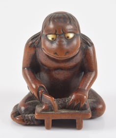 Carved toggle. Japan. 19th century. Netsuke of Tengu with inlaid eyes preparing a fish for cooking.