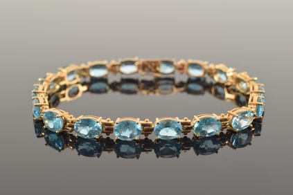14K gold blue topaz mounted bracelet. Set with 18 oval cut stones. Marked 585. 7in length. 13.1