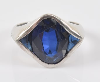 White gold synthetic sapphire mounted ring. Oval cut stone flanked by trillion style cut sapphires.
