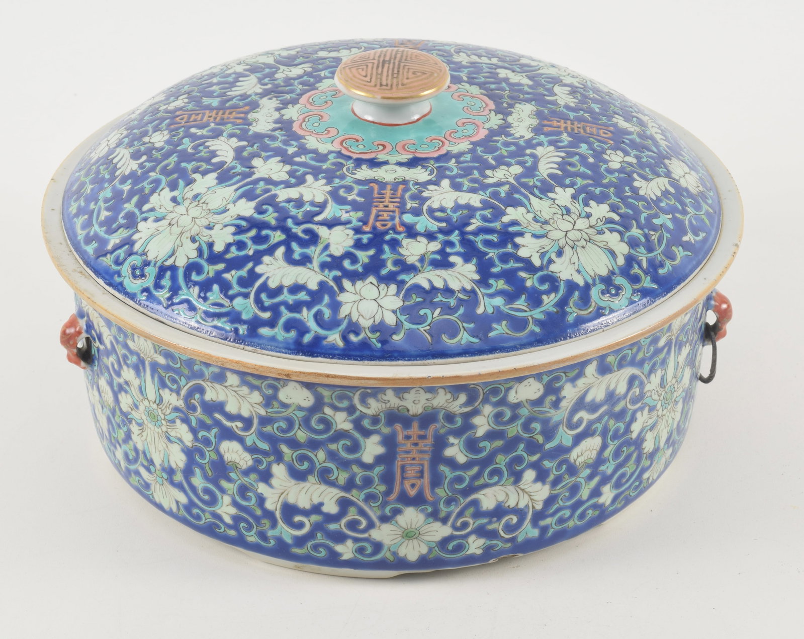 Porcelain covered bowl. China. 19th century. Cobalt blue ground decorated with stylized floral: Porcelain covered bowl. China. 19th century. Cobalt blue ground decorated with stylized floral scrolling. Several small glaze chips on side of rim. Metal bail missing from one handle. 11.5in diameter.