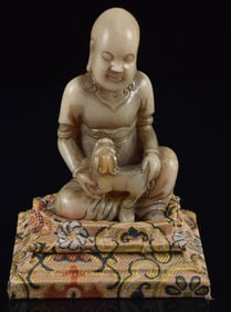 Soapstone carving of a Luohan with a lion cub. China. 20th century. Silk stand. 3in.