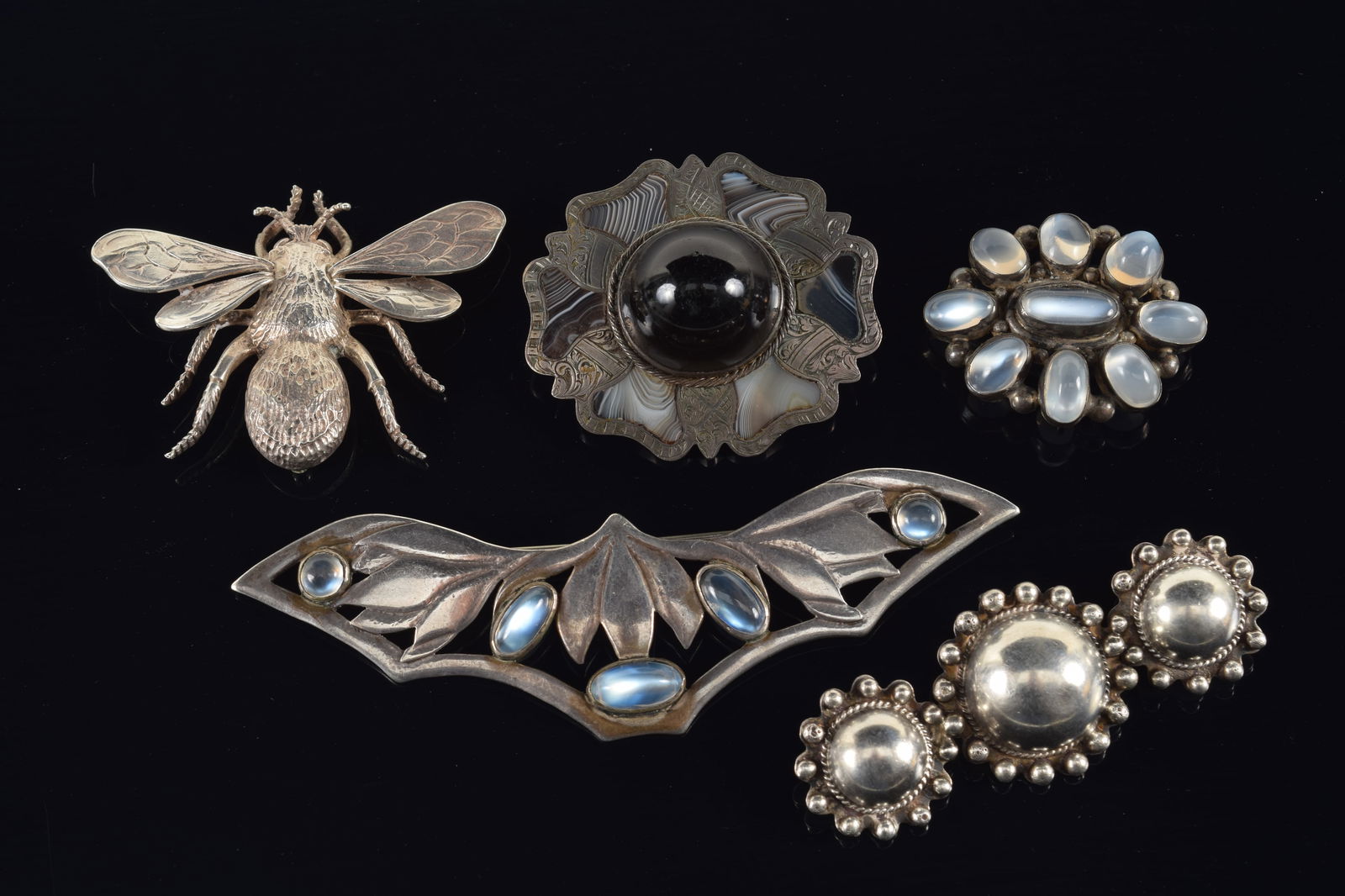 5 vintage designer silver pins. 1) Pierced floral design large pin set with 5 moonstones. "D": 5 vintage designer silver pins. 1) Pierced floral design large pin set with 5 moonstones. "D" maker's mark on reverse. 4.5in wide. 2) Antique silver brooch inset with agate trefoils surrounding a blac