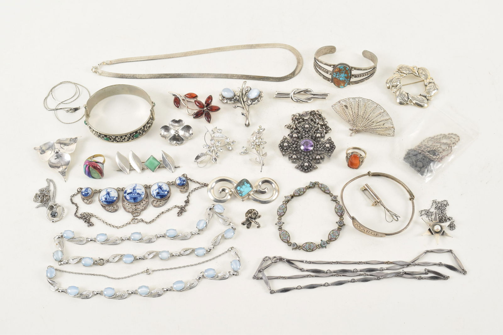 Large assortment of silver jewelry. To include: 2 Danecraft pins, one floral pin mounted with: Large assortment of silver jewelry. To include: 2 Danecraft pins, one floral pin mounted with moonstones; Jerusalem silver cross pendant necklace; Several turquoise mounted pieces; Italy green stone m