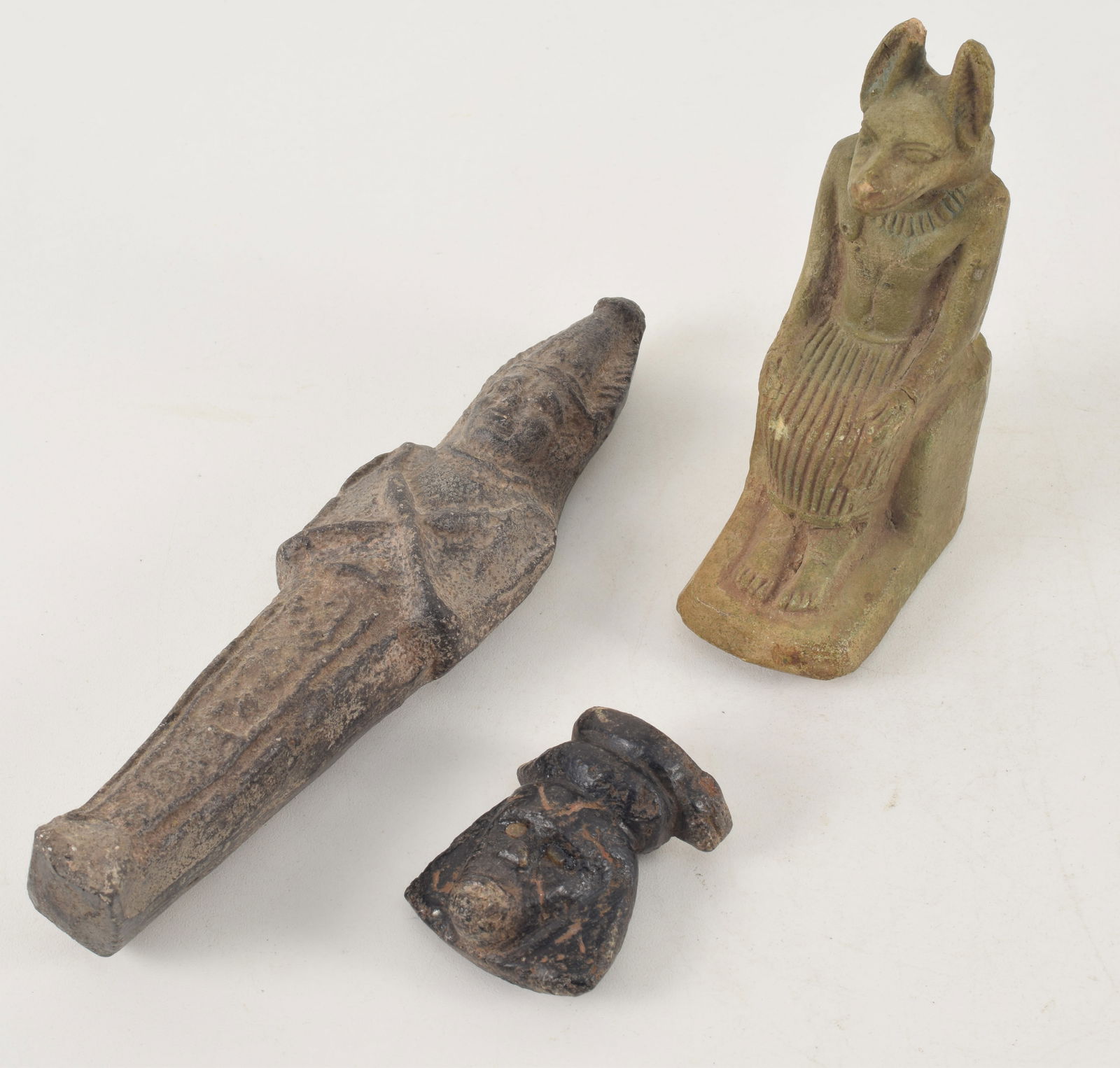 3 Egyptian items. 1) Seated green glazed figure. 4.5in high. 2) Small black stone carved head with: 3 Egyptian items. 1) Seated green glazed figure. 4.5in high. 2) Small black stone carved head with coiled snake. 2in high. 3) Tall standing carved figure. 7.25in high. Provenance: From a Massachusetts