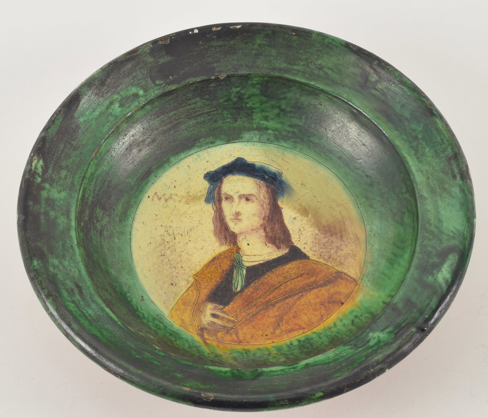 Renaissance glazed terracotta deep dish with majolica style decoration of a figure in cloak and hat.: Renaissance glazed terracotta deep dish with majolica style decoration of a figure in cloak and hat. Initialed and dated to the left of figure. Glaze imperfection to the right of the figure. 12.5 diam