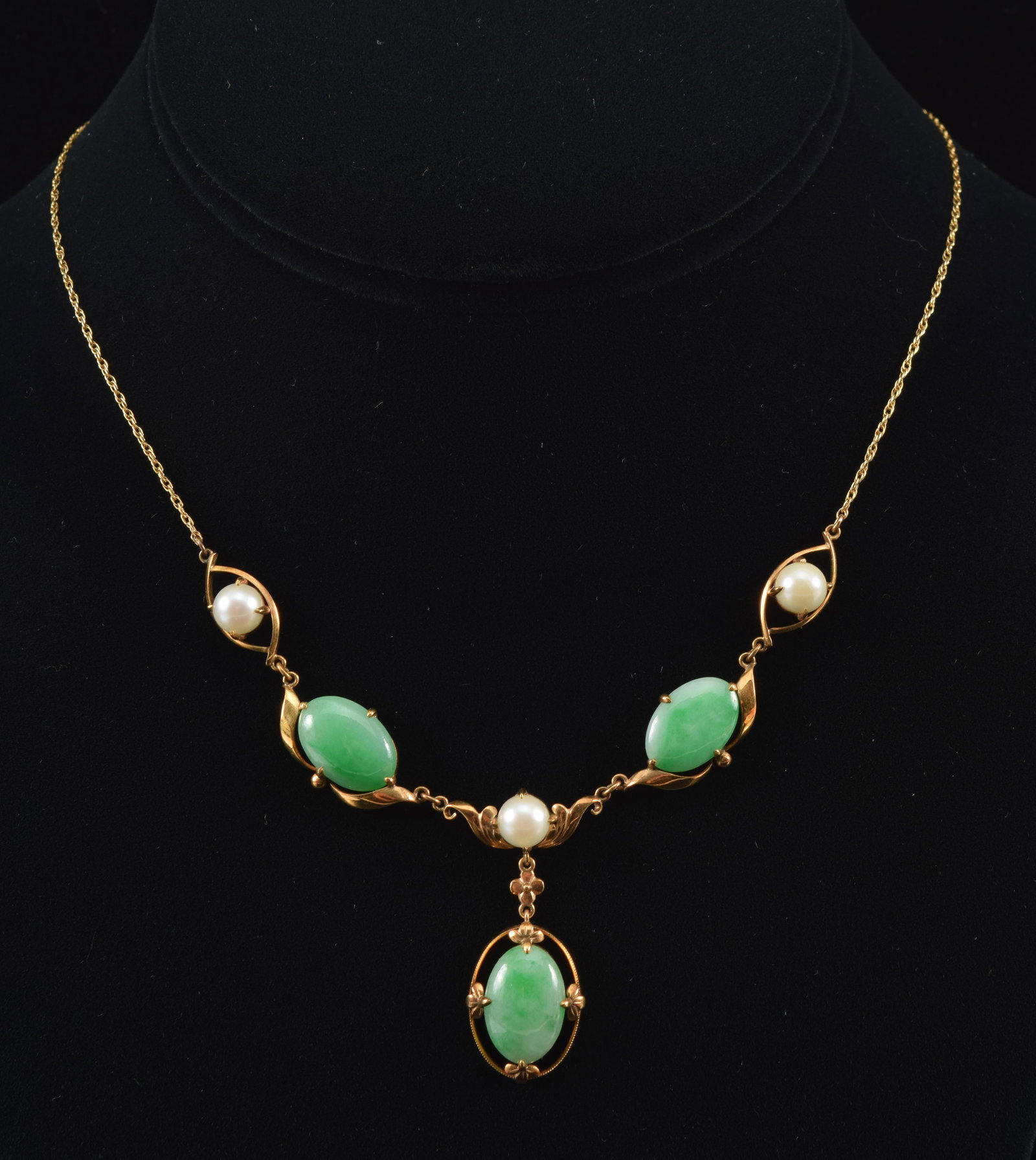 14K gold jade and pearl mounted necklace. Ribbon and scroll setting of alternating pearls and oval: 14K gold jade and pearl mounted necklace. Ribbon and scroll setting of alternating pearls and oval jade cabochons with a single drop pendant mounted with jade. Jade of a mottled green apple and celado