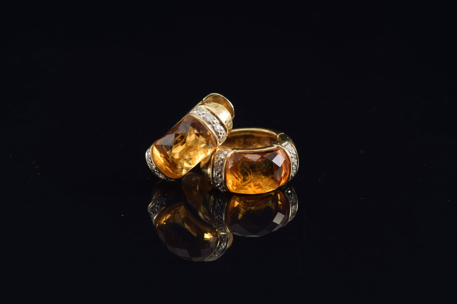 14K gold citrine and diamond huggie earrings. Faceted citrine stones with bands of small round cut: 14K gold citrine and diamond huggie earrings. Faceted citrine stones with bands of small round cut diamonds set in white gold on either side. Marked 14K. 5/8in wide. 5.7 grams.