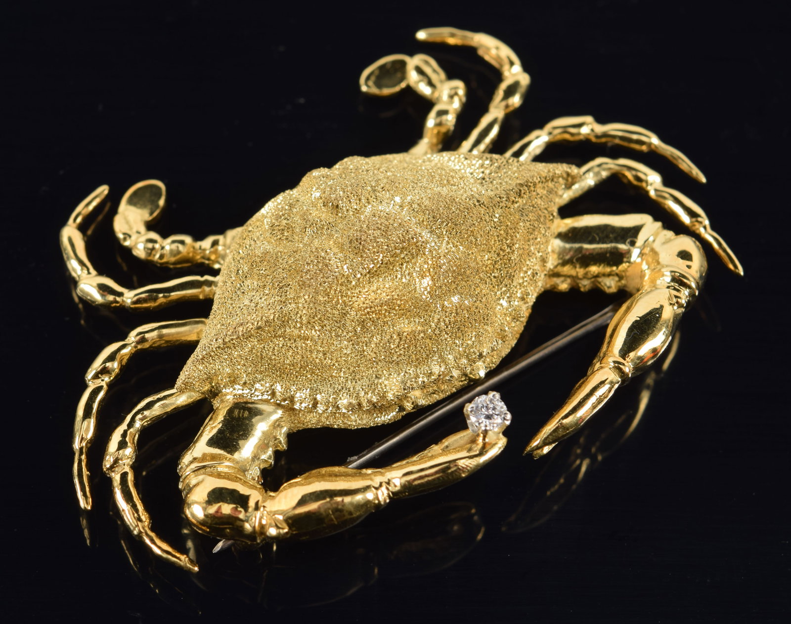 18K gold heavy crab form pin. Crab depicted with a realistic textured shell surface and clasping a: 18K gold heavy crab form pin. Crab depicted with a realistic textured shell surface and clasping a single round cut diamond in his claw. Stamped 18K on interior of shell. 2 1/8in wide. 23.6 grams.