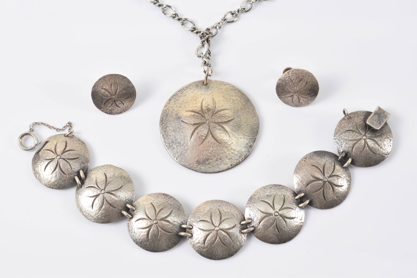 Clifford Russell. Maine. Sterling silver sand dollar jewelry suite. Pendant necklace (chain length: Clifford Russell. Maine. Sterling silver sand dollar jewelry suite. Pendant necklace (chain length 25in), pair of earrings, and bracelet (8.5in length). Pendant signed. 2.6 ozt total weight.