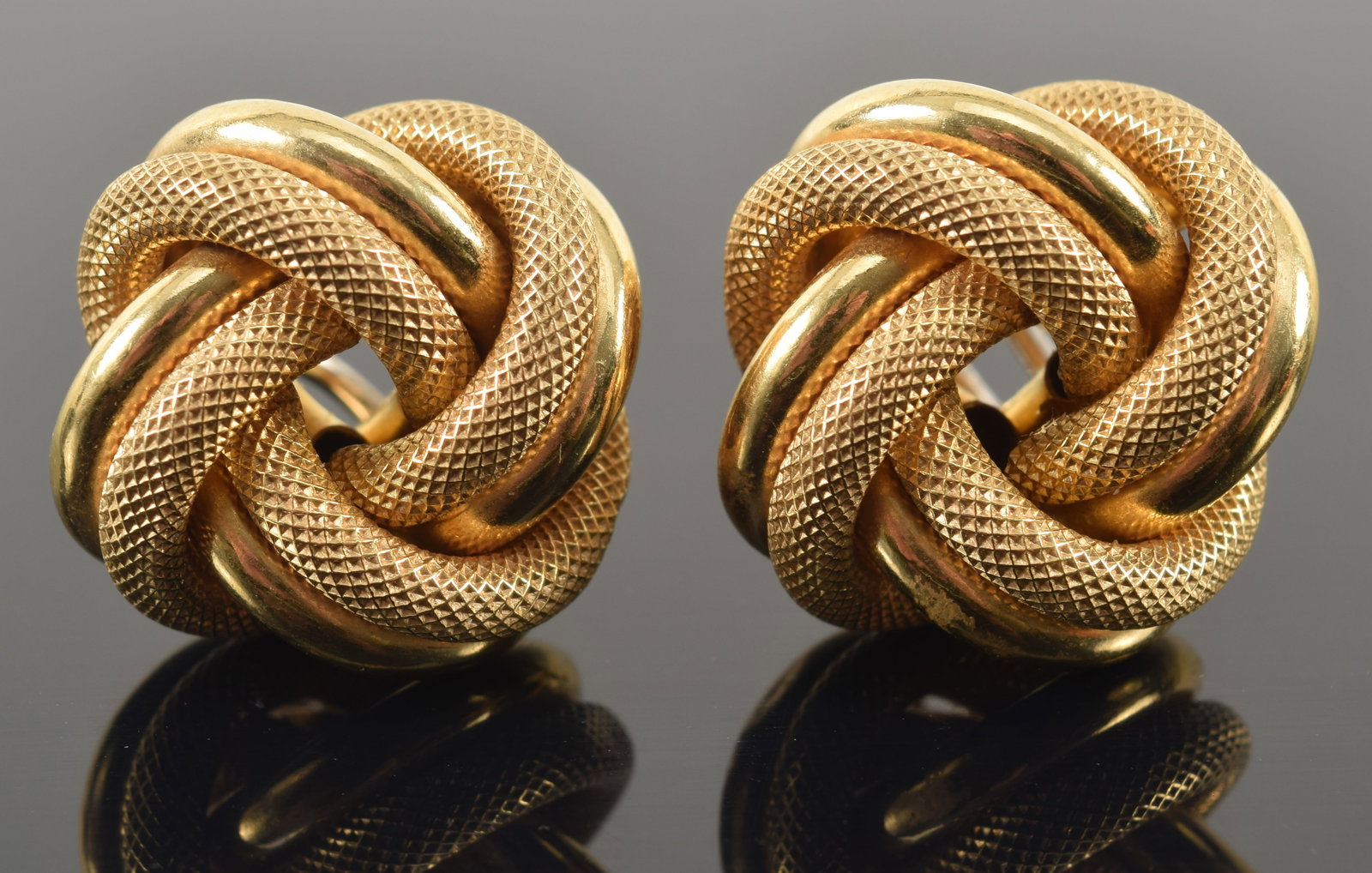 Unoaerre 14K gold love knot earrings. 2 interlocked strands, one with a polished surface, the other: Unoaerre 14K gold love knot earrings. 2 interlocked strands, one with a polished surface, the other with a crosshatch textured surface. Marked on reverse. 1in diameter. 11.3 grams.