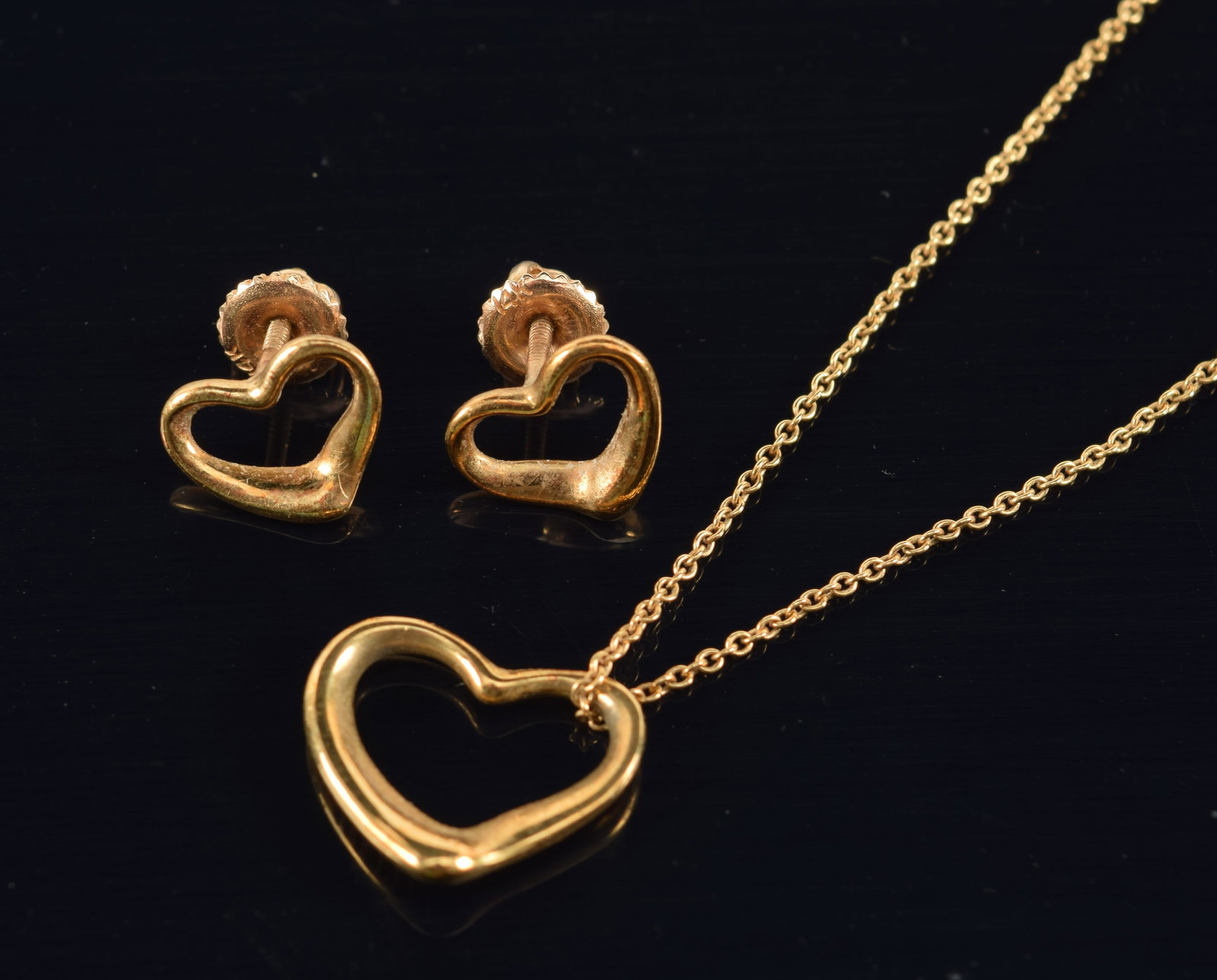 Elsa Peretti for Tiffany & Co. 18K gold open heart necklace and earring set. Chain marked near: Elsa Peretti for Tiffany & Co. 18K gold open heart necklace and earring set. Chain marked near clasp. Back of heart pendant marked. Earrings marked on reverse. 15in chain length. 4.5 grams.