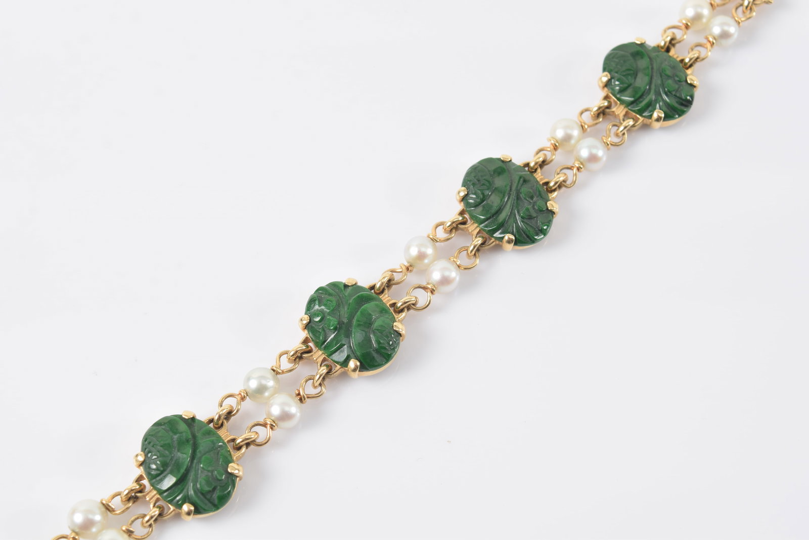 14K gold pearl bracelet. Floral carved green stone medallions on dual strand gold link chain with: 14K gold pearl bracelet. Floral carved green stone medallions on dual strand gold link chain with pearls. Marked on clasp. 6.25in length. 17.4 grams.