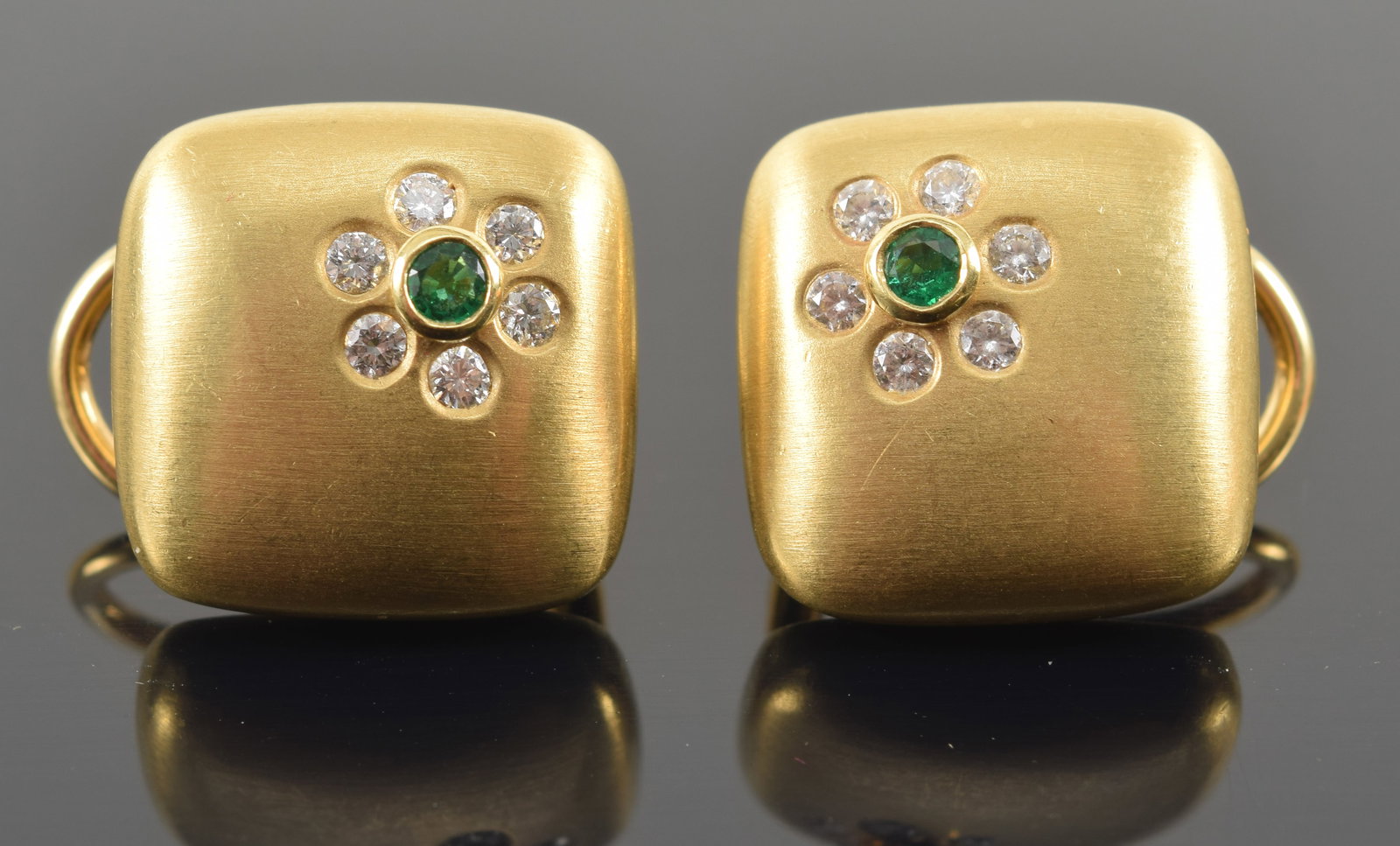 Suna 18K gold diamond and emerald pillow form earrings. Brushed finish. Floral form stone setting: Suna 18K gold diamond and emerald pillow form earrings. Brushed finish. Floral form stone setting with emerald center. Emerald measures approx. 2.2mm diameter. Marked Suna, 18K and serial number on re