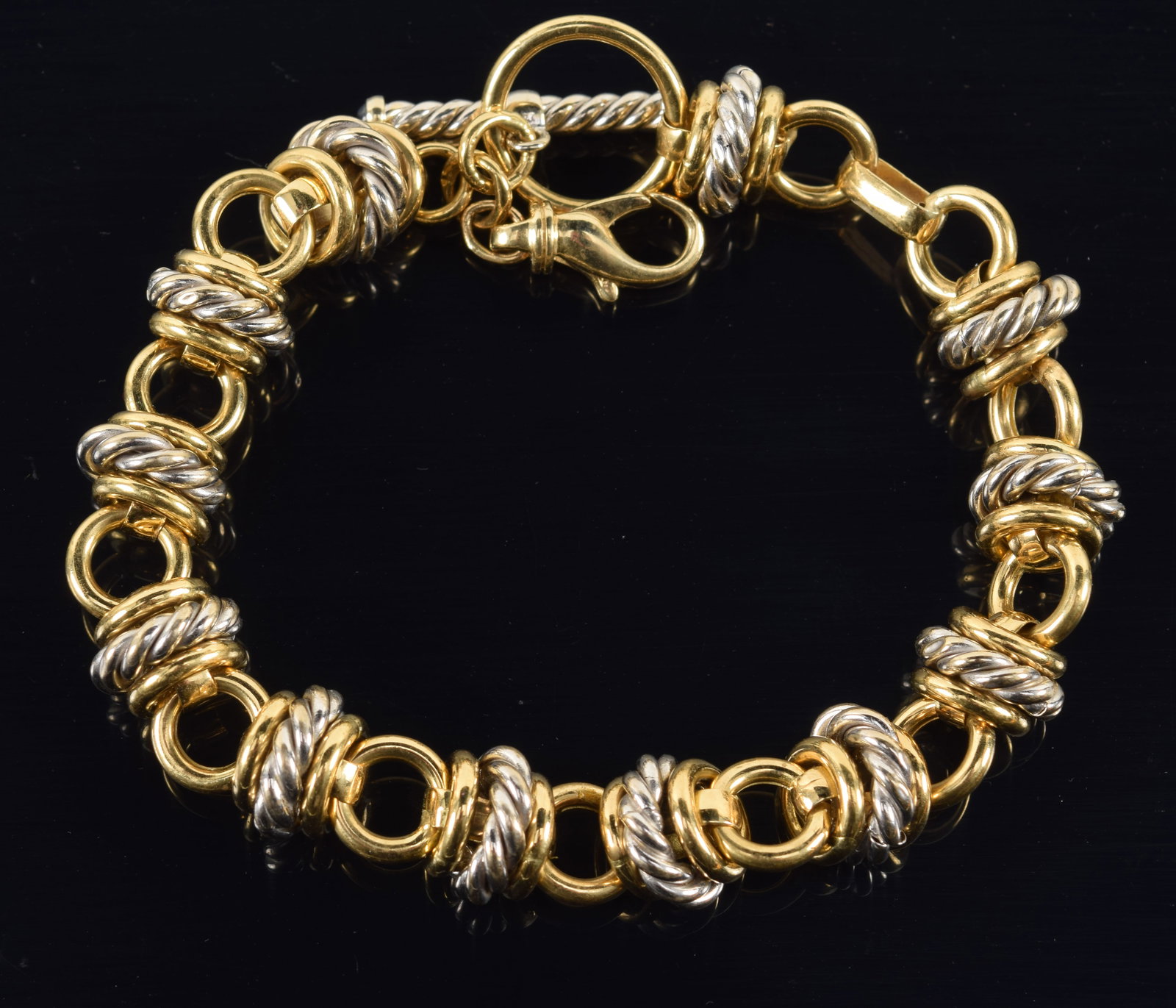 18K white and yellow gold heavy ring link bracelet. Pattern of polished yellow gold rings flanking: 18K white and yellow gold heavy ring link bracelet. Pattern of polished yellow gold rings flanking larger braided white gold rings. Toggle and lobster claw clasps. Toggle decorated with blue enamel ac