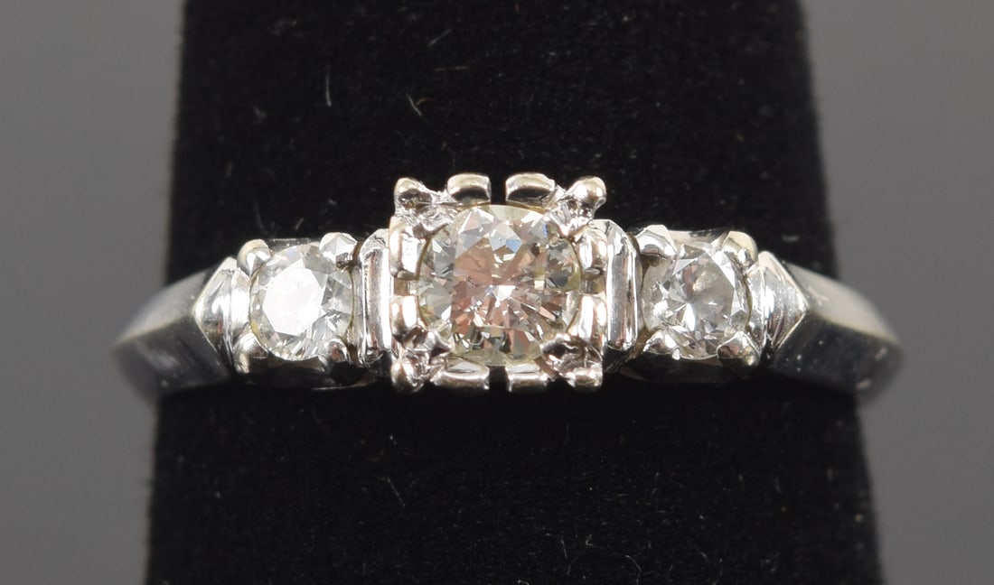 18K white gold diamond ring. Center diamond approx. 3.6mm diameter. Flanked by two smaller diamonds: 18K white gold diamond ring. Center diamond approx. 3.6mm diameter. Flanked by two smaller diamonds (each about 2.6mm), one of lesser quality. Marked 18K. Ring size 6.5. 2.5 grams.