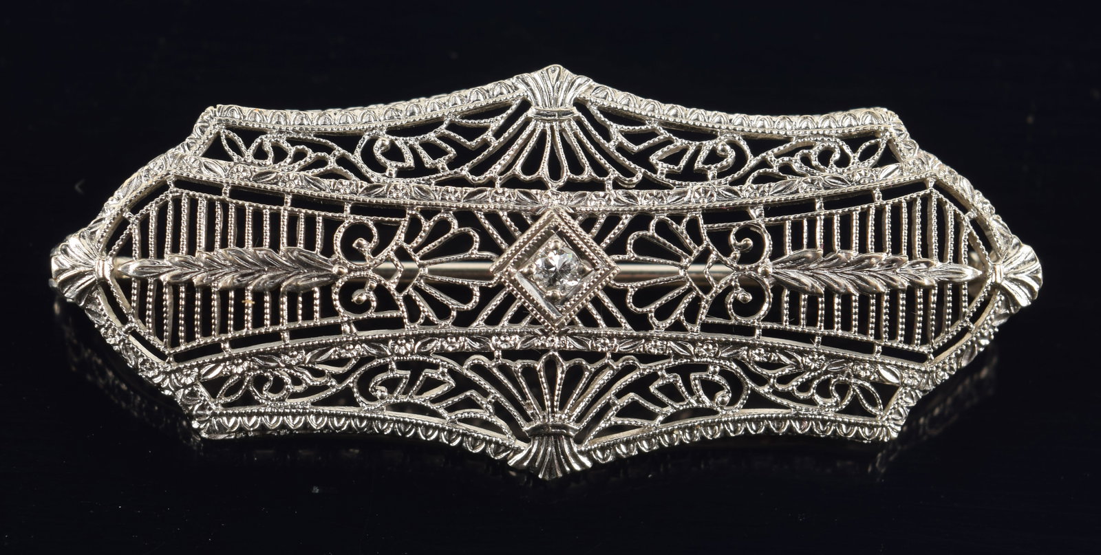 14K white gold art deco diamond pin. Open filigree design with bright cut panels. Central small: 14K white gold art deco diamond pin. Open filigree design with bright cut panels. Central small round cut diamond. Clasp hinge marked. 1 7/8in length. 3.5 grams.