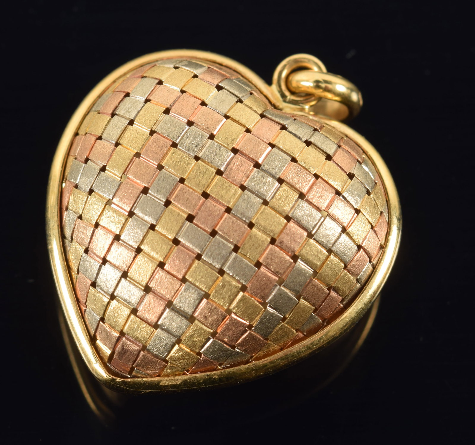 18K gold heart form pendant with woven tri-color gold design on one side, and brushed yellow gold: 18K gold heart form pendant with woven tri-color gold design on one side, and brushed yellow gold finish on the other. Marked. 1in wide. 6.1 grams.