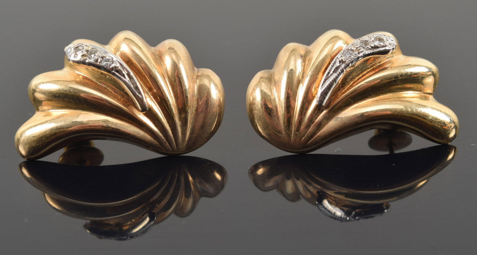 14K gold ribbed wave form earrings. Raised white gold diamond mounted accent. Posts marked 14K. 1in: 14K gold ribbed wave form earrings. Raised white gold diamond mounted accent. Posts marked 14K. 1in length. 4.9 grams.