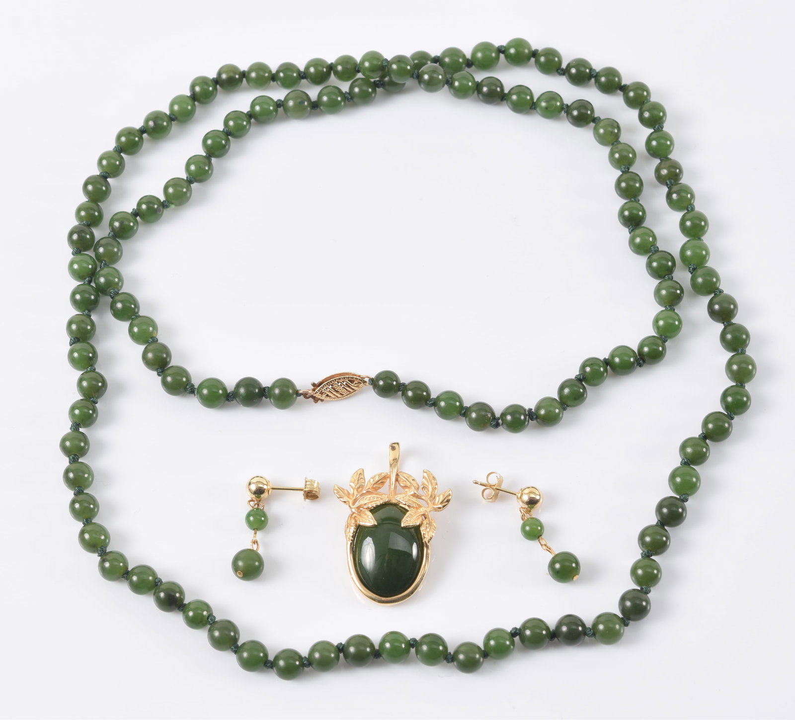 Gold jade jewelry. To include: 1) Dark green jade oval cabochon in foliate 14K gold setting pendant. (1 of 4)