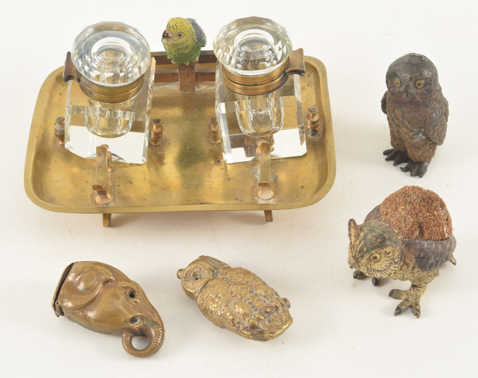 Collection of miniature novelties including a cold painted bronze owl form pen wipe, a brass pen: Collection of miniature novelties including a cold painted bronze owl form pen wipe, a brass pen tray with a painted parrot and inkwells, two owls, one as match safe and an elephant form match safe.