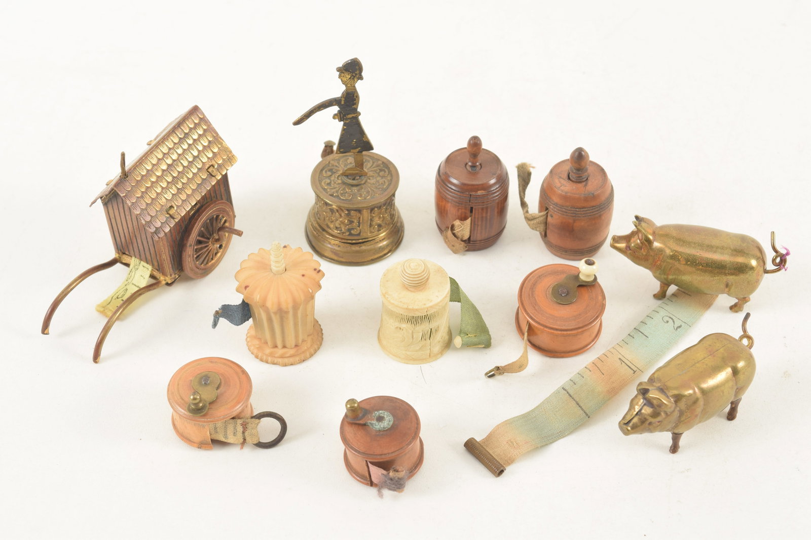 Collection of 11 miniature tape measures including 5 treenware, 2 carved, 2 cast brass pigs, a: Collection of 11 miniature tape measures including 5 treenware, 2 carved, 2 cast brass pigs, a traffic policeman and a wheeled cart.