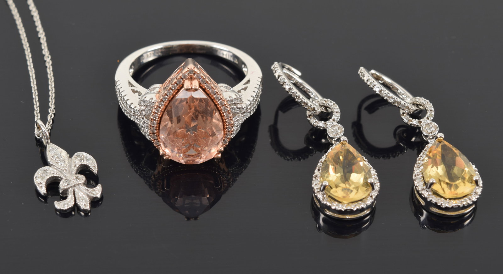 Sterling silver jewelry. To include: 1) Pair of citrine pear shaped dangle earrings with tiny diamon: Sterling silver jewelry. To include: 1) Pair of citrine pear shaped dangle earrings with tiny diamond settings. 2) Sterling silver ring with glass stone in morganite coloring. 3) Small fleur-de-lys pe