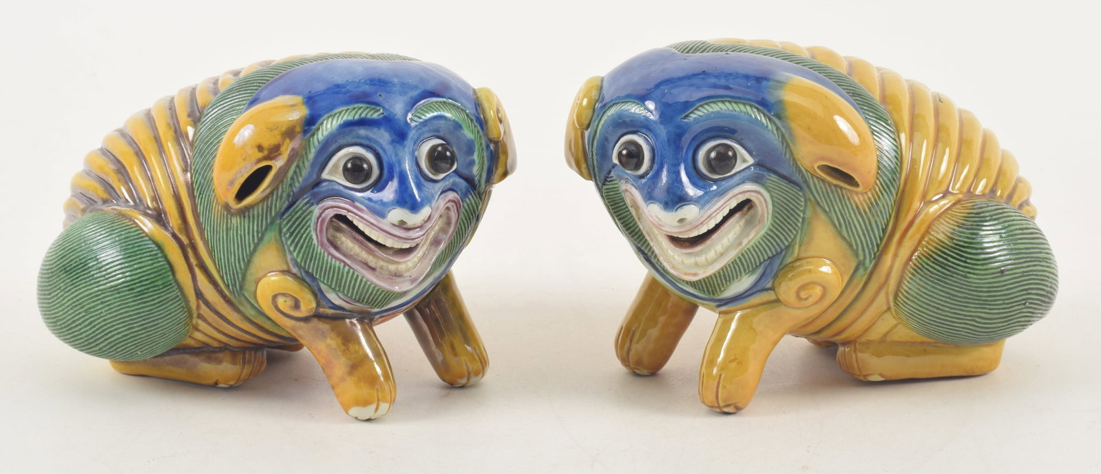 Pair of 19th century or earlier Chinese porcelain buddhist lions with carved facial features. Finely: Pair of 19th century or earlier Chinese porcelain buddhist lions with carved facial features. Finely modeled. Sancai glaze and blue mask faces. Minor glaze chips on underside of some feet. 6in length.