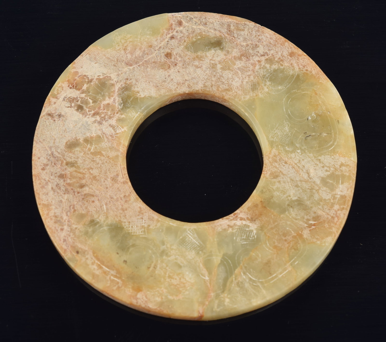 Jade pi disc. China. Carved archaic decoration. Calcified celadon colored stone with brown markings. (1 of 3)